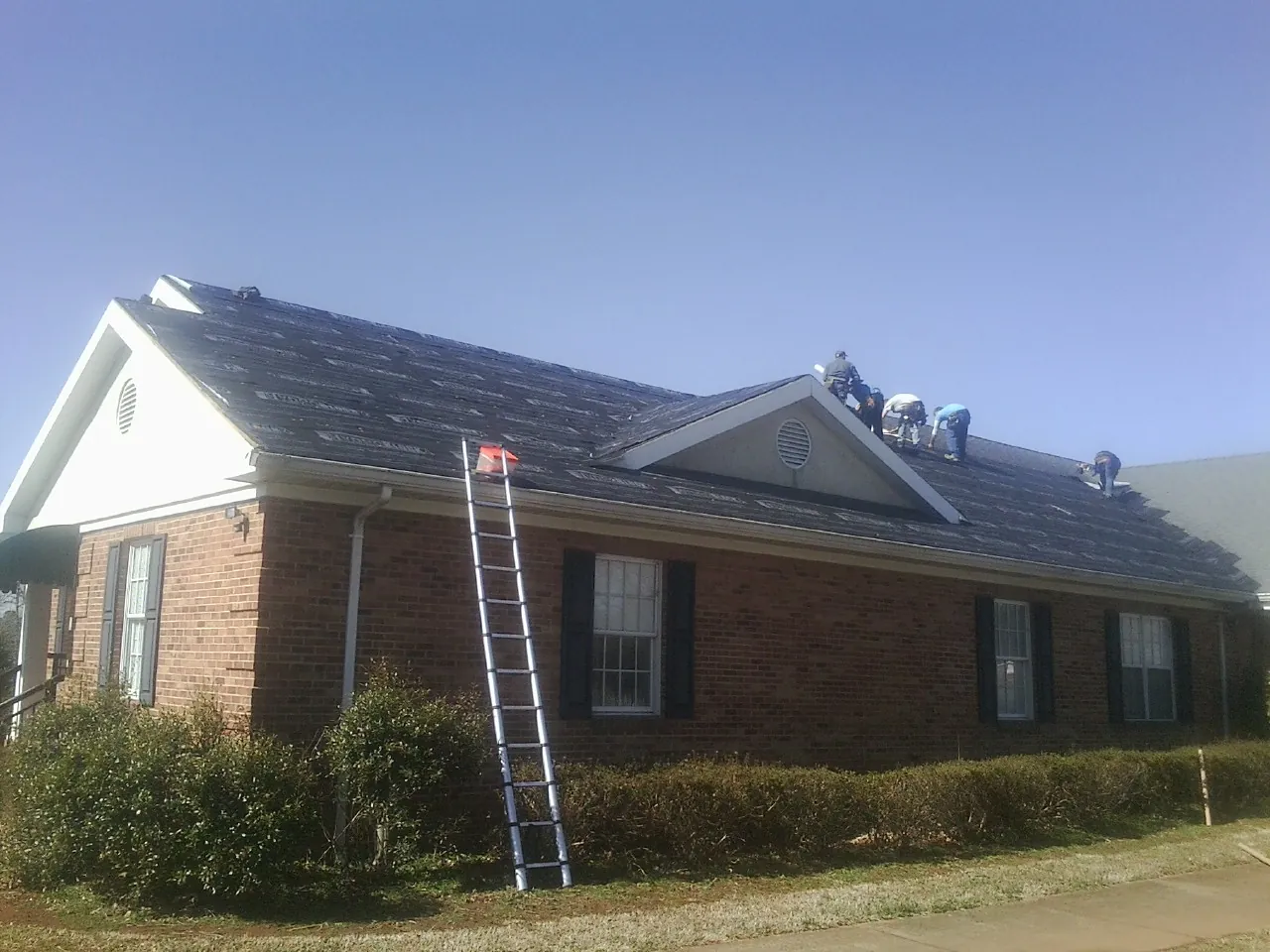 Crew tearing shingles off a brick ranch roof with a ladder set — Metal Roof Repair work by our crew in Rancho Cordova