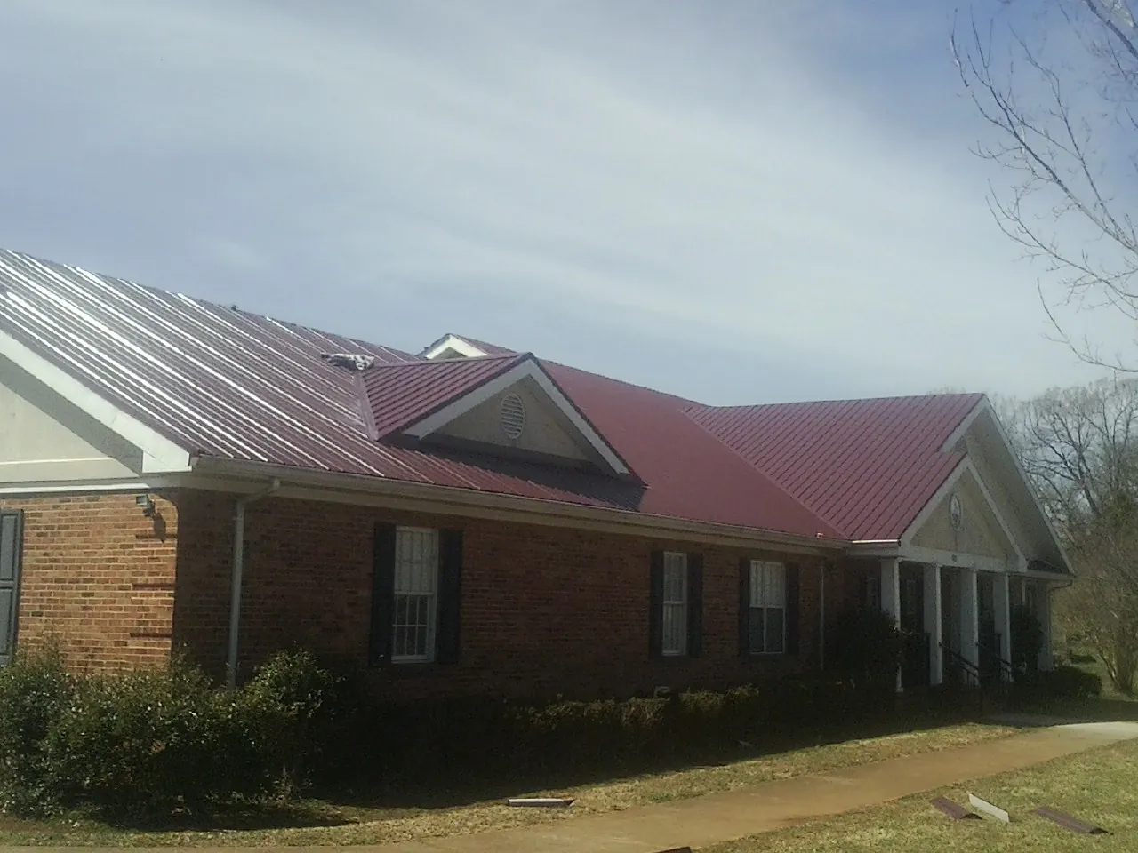 Red metal roof with gabled entries on a long brick building, from a Hail Damage Roof Repair job in Rancho Cordova