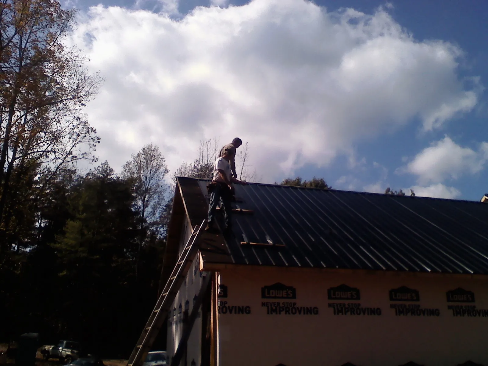 Roofer fastening dark metal panels high against a cloudy sky, from a Roof Inspection job in Rancho Cordova