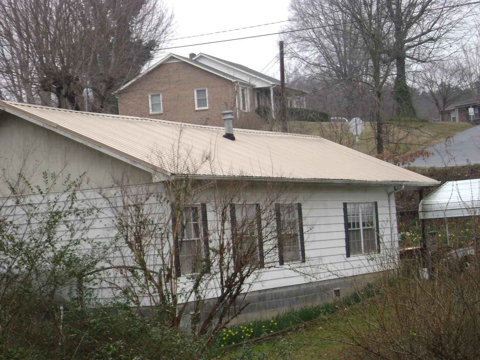 Tan metal roof on a white sided house set into a hillside — Commercial Roofing by Roofing Brothers in Rancho Cordova